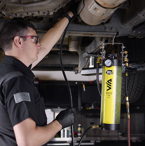 Technician under a lifted vehicle using the 1G Emissions Service VIA®
