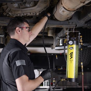 Technician under a lifted vehicle using the 1G Emissions Service VIA®